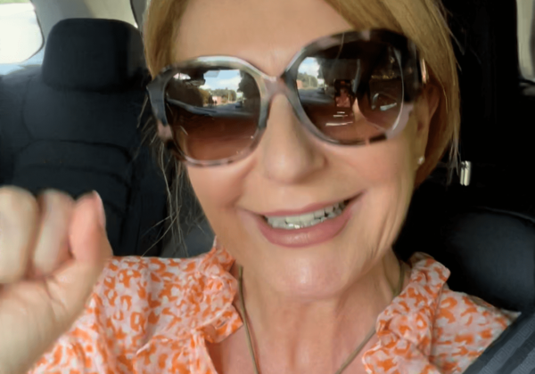 Woman smiling in car, wearing sunglasses.