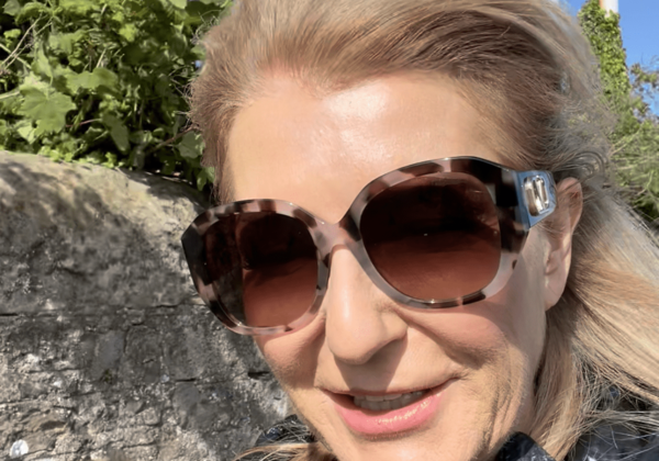 Woman wearing sunglasses outdoors, smiling in sunlight.