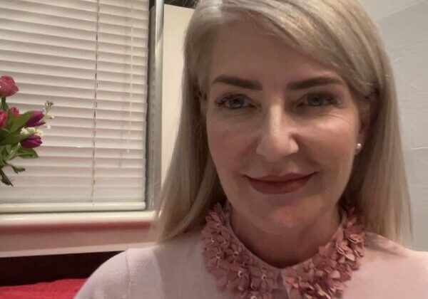 Smiling woman in pink sweater, flowers nearby.