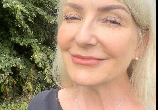 Smiling woman outdoors with green foliage background.